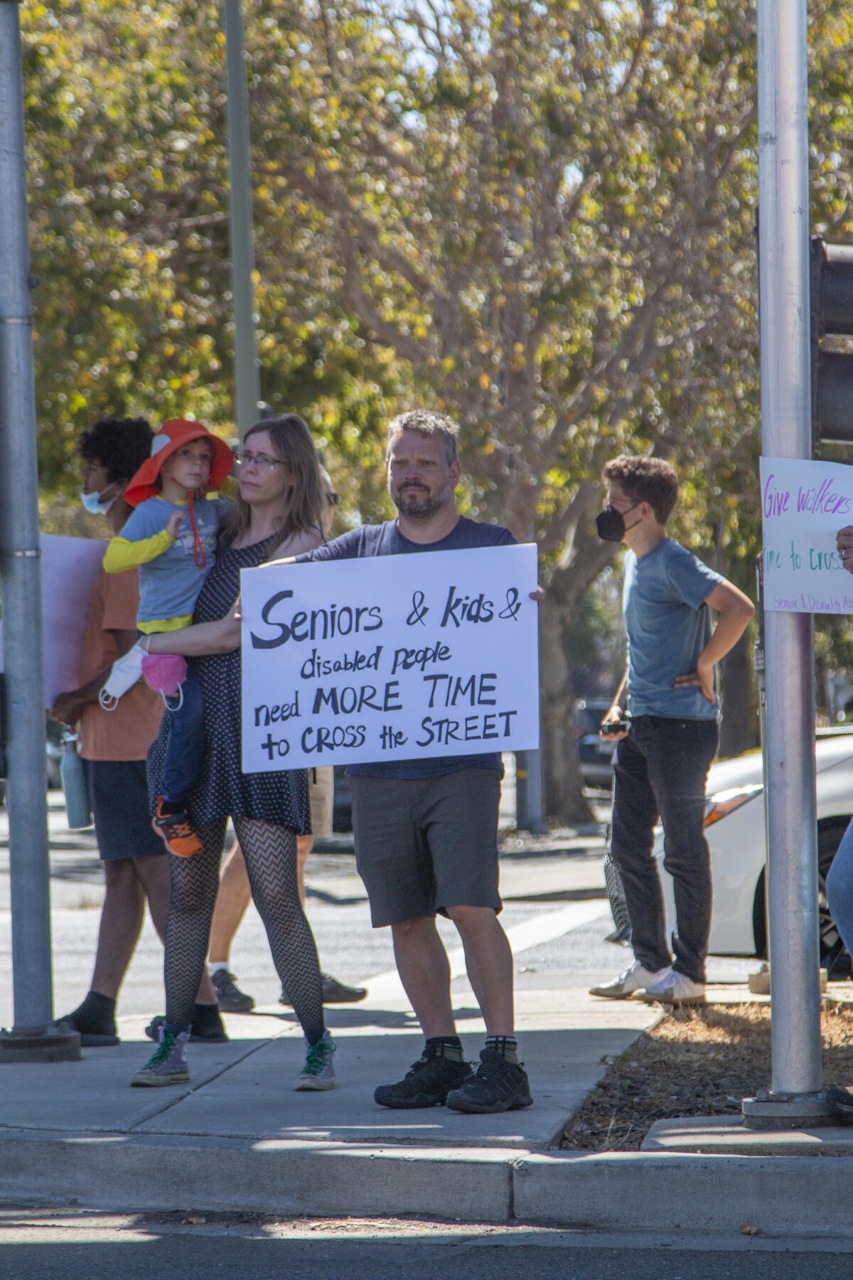 An activist holds a sign "Seniors & kids & disabled people need more time to cross the street."