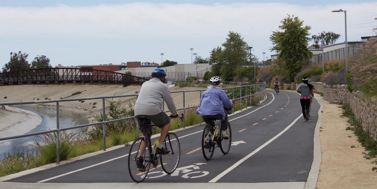 People ride bikes and jog on a separated, multi-use bicycle path.