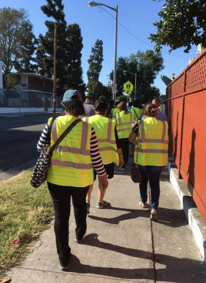 A group of people wearing bright yellow safety vests walk along a sidewalk.
