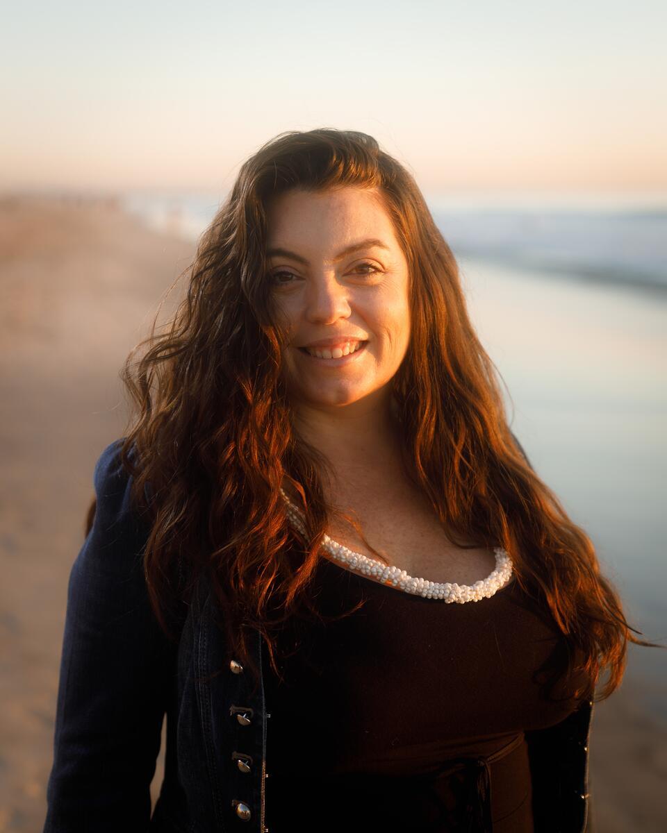 Pualani smiles at the camera, a beach is in the background