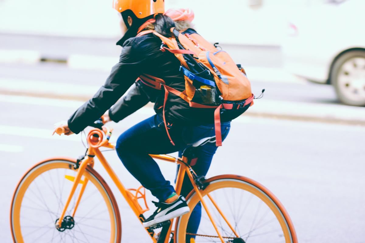 Photo of cyclist wearing orange helmet on a bicycle.