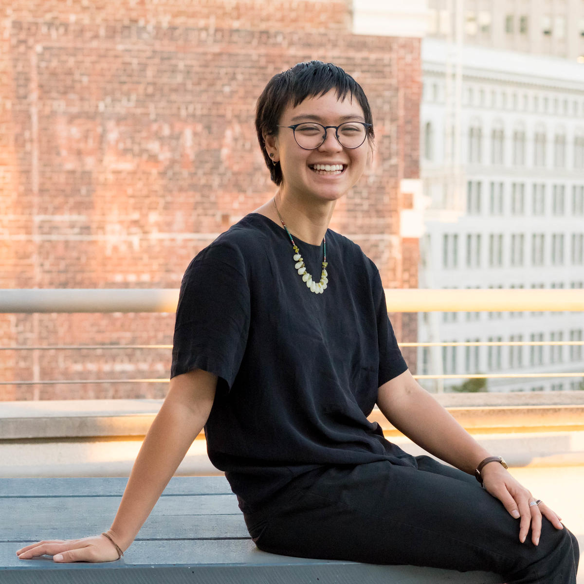 A woman with very short brown hair smiles while wearing a black dress.