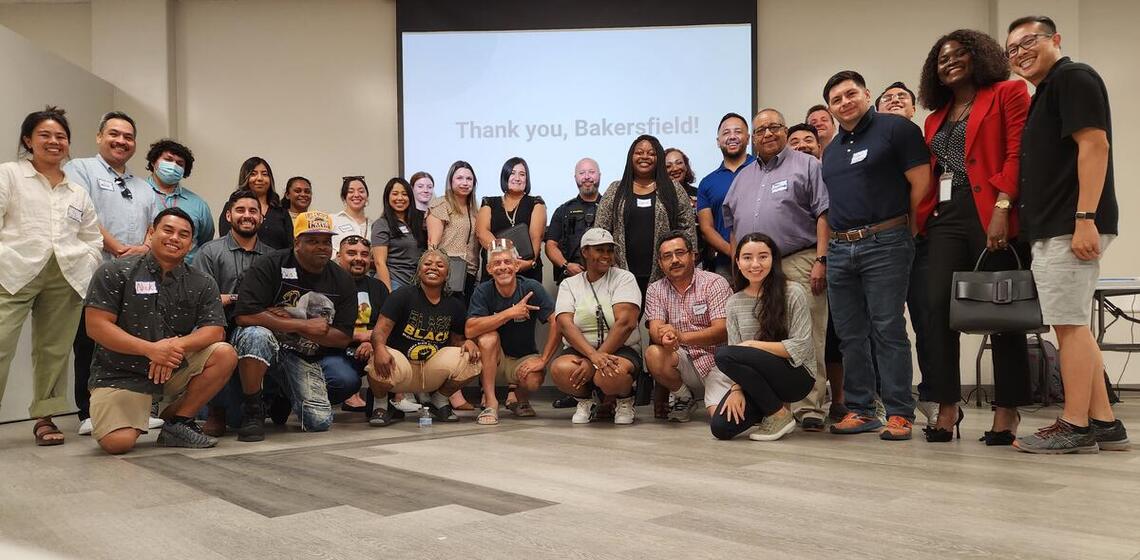 A large group of workshop participants stand and smile at the camera.