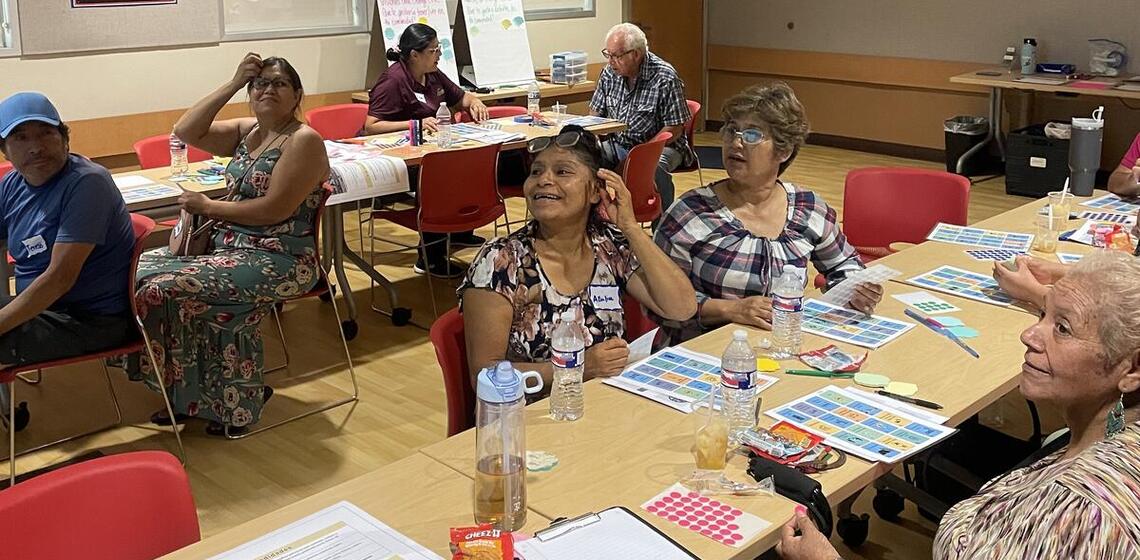 Seven workshop participants sit at tables during a workshop activity.