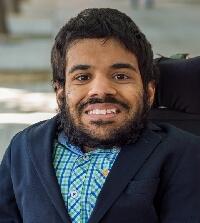 A photo of Prashanth, sitting in a powerchair and smiling at the camera. 