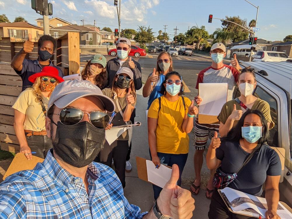 Circulate San Diego Community Event on city street with participants, all wearing masks, facing the camera with a thumbs up
