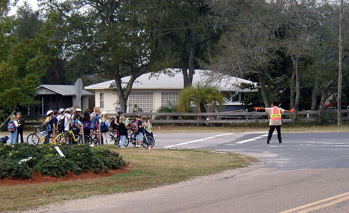 Crossing guard signaling for traffic to stop at an intersection for a group of young students walking and biking 