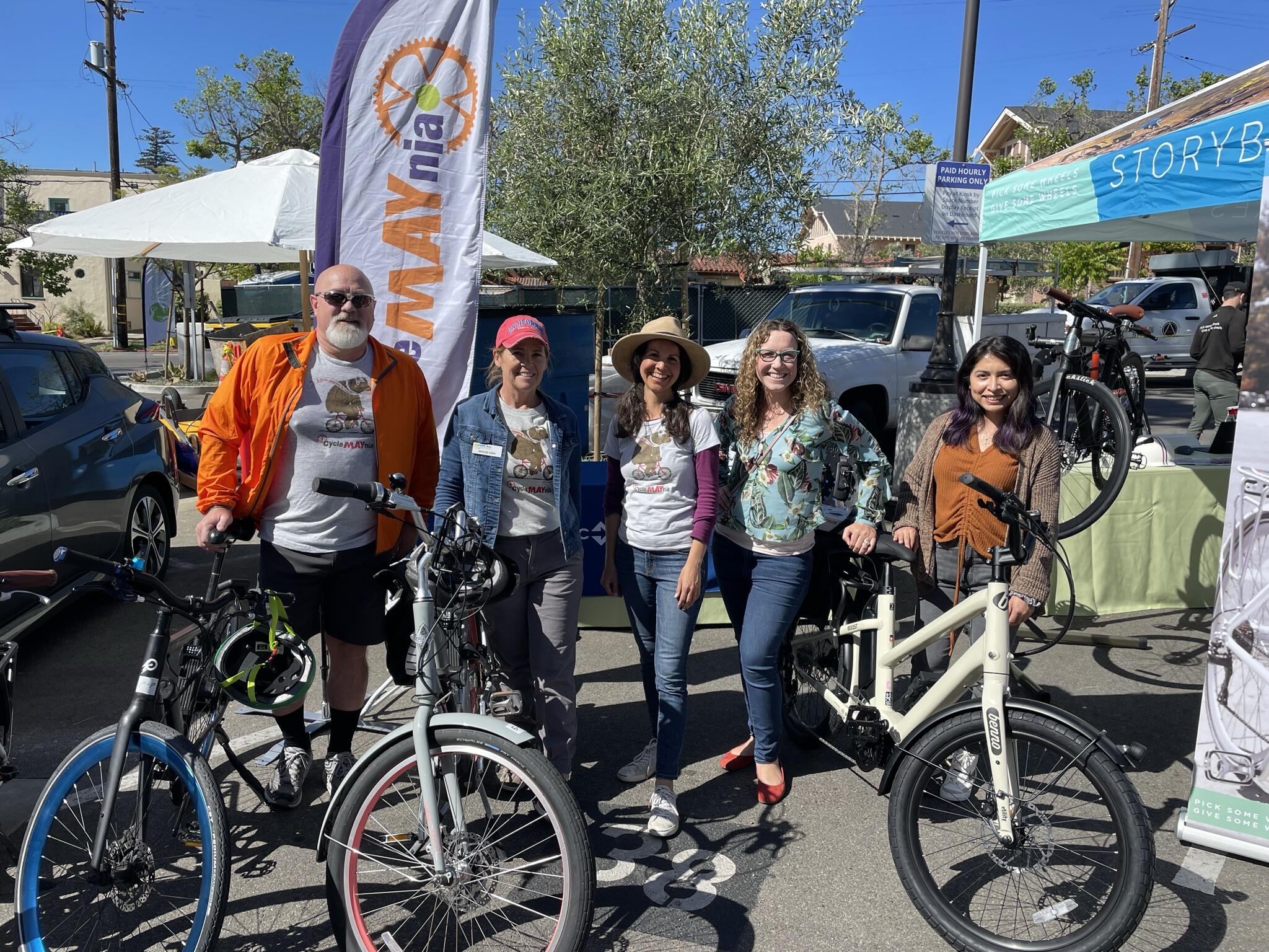 A group of people smile at a camera, a fleet of electric bikes sits in front of them. 