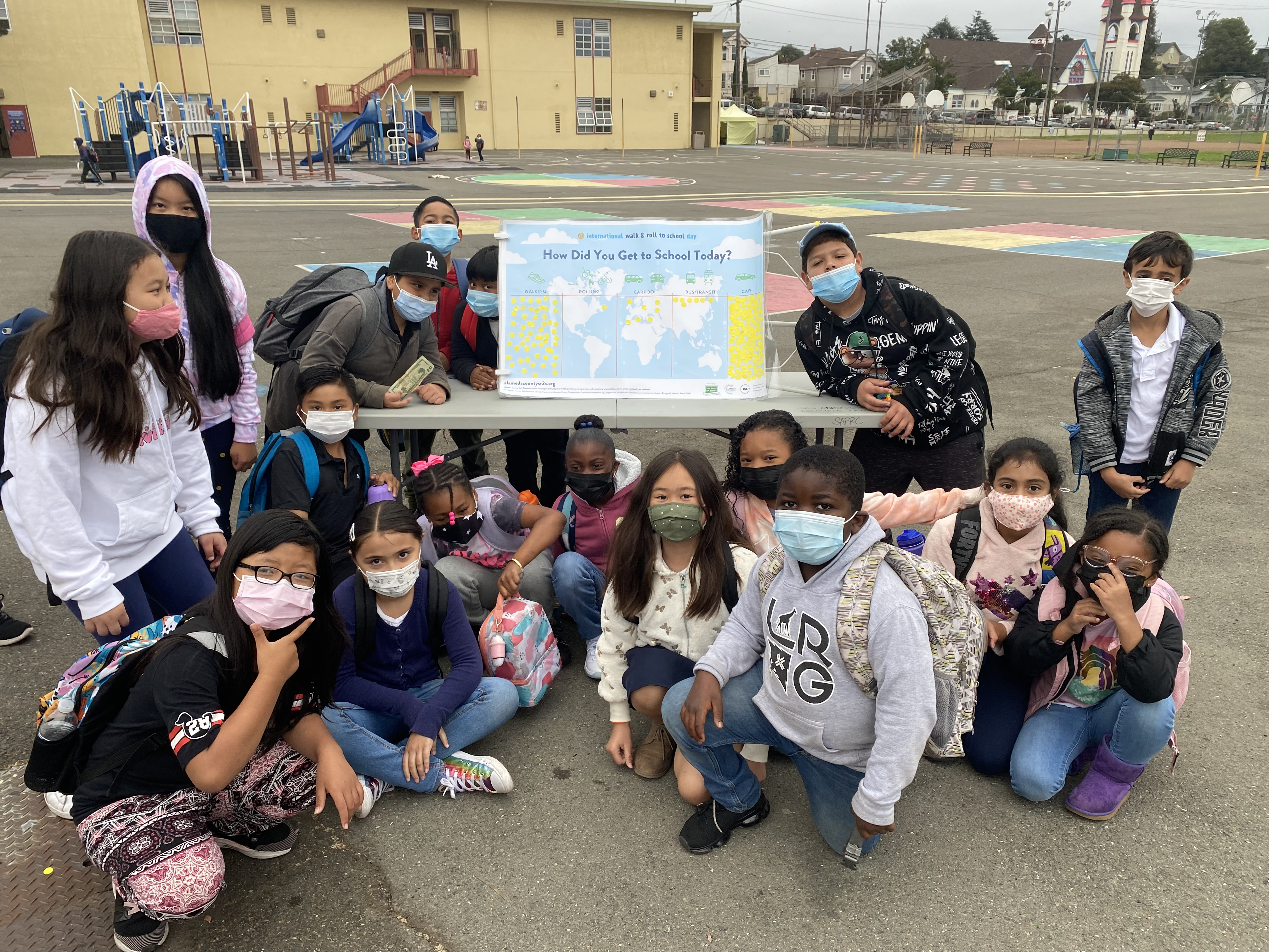 A group of children smile while masked on a courtyard on International Walk and Roll to School Day.