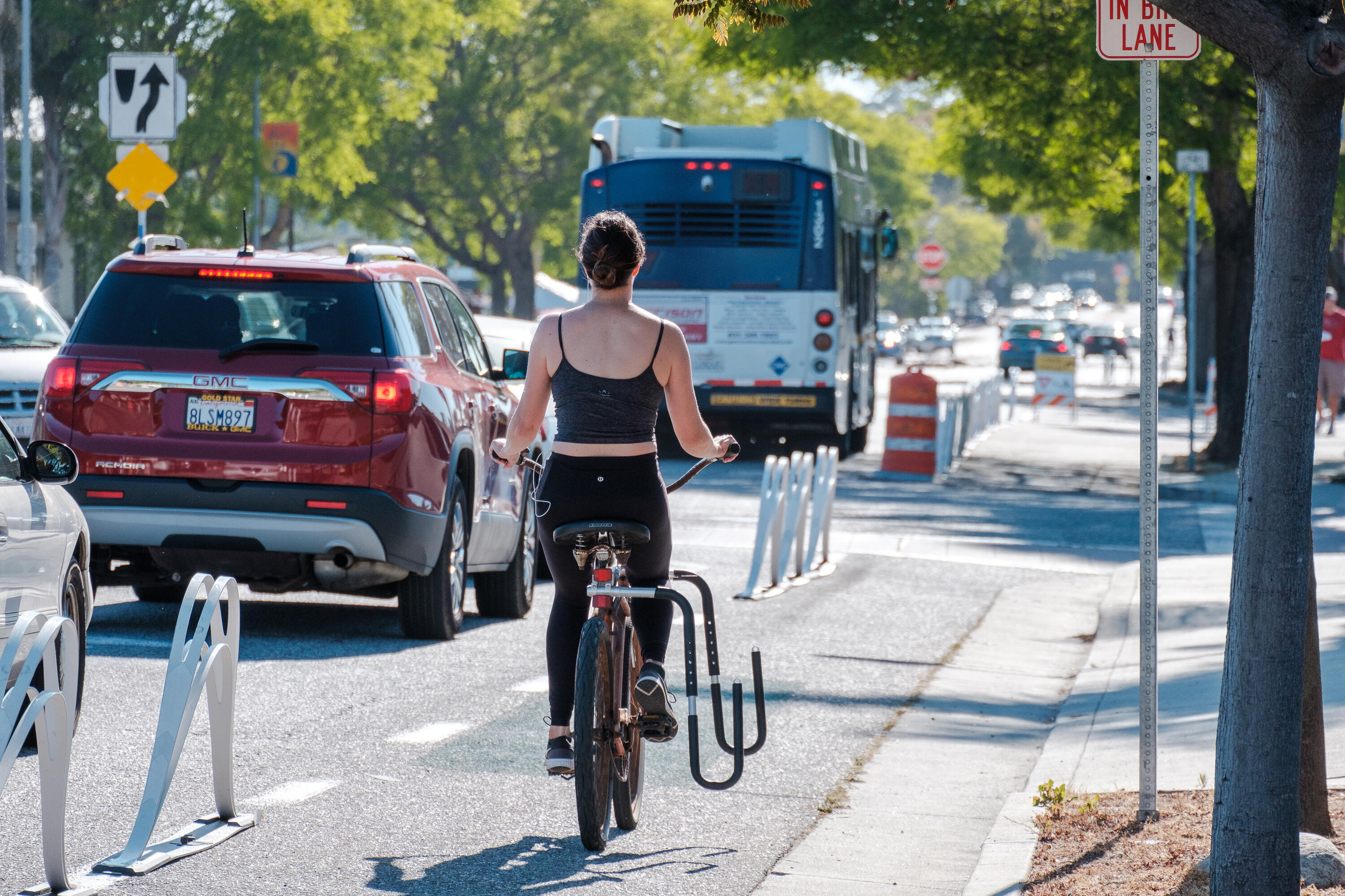 A person biking on the Portola pop-up bike lane, there are cars and a bus next to the bike lane along the street