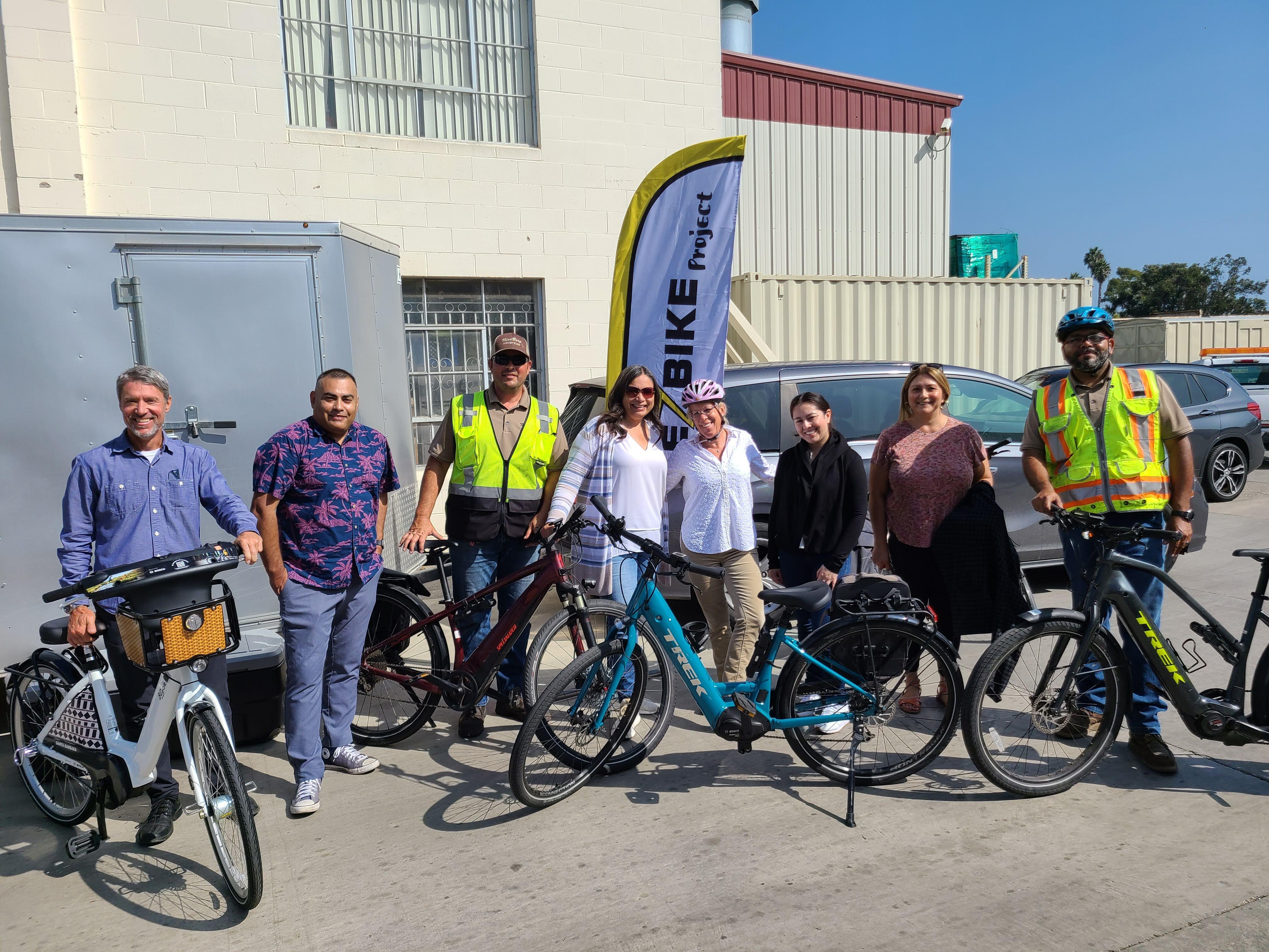 A group of people smiling, there is a fleet of electric bikes in front of them. 