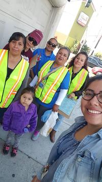 A group of women and one young girl pose for a photo. Three are wearing safety vests and holding clipboards.